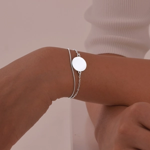 Close-up of a double-layer stainless steel chain bracelet with a polished round disc pendant