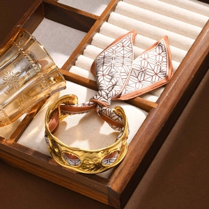 Detail eines goldenen Armreifs mit Seidenschal auf einer hölzernen Schmuckschatulle