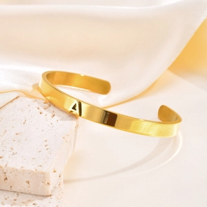 Primer plano de pulsera rígida dorada pulida con un detalle minimalista de la letra A central