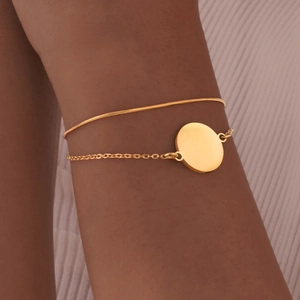 Detail of a double-layer gold chain bracelet with a polished round pendant on skin
