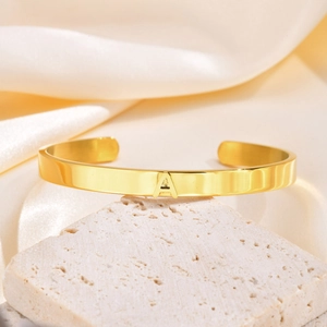 Detalle de brazalete abierto de acero inoxidable dorado con adorno de la letra A inicial