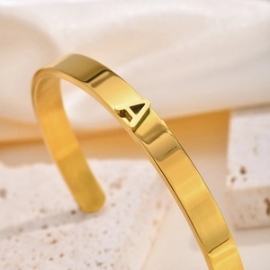 Detalle de brazalete de acero inoxidable dorado con un dije de la letra A pulida
