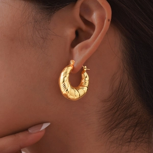 Macro shot of gold twisted hoop earring with spiral texture shown on model's ear