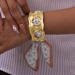 Detail eines goldenen Hammerschlag-Armreifs mit elegantem braunem Seidenschal-Dekor
