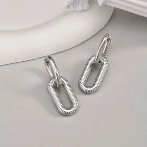Close-up of silver oval hoop earrings with horizontal textured grooved metal surface