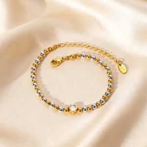 Detail van K18 kralenarmband met hartvormige zirkoon op champagnekleurige zijde