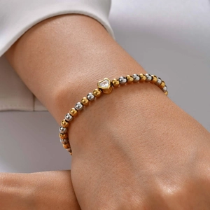 Detail van een kralenarmband met goud-zilveren kralen en een hartvormige zirkoon hanger