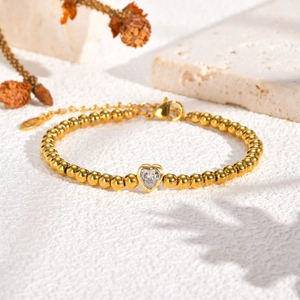 Detail van goudkleurige kralenarmband met hartvormige zirkoon en verstelbare sluiting