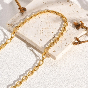 Detail of gold-plated twisted link chain necklace on textured white stone with pine cone