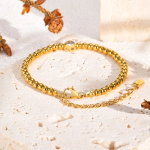 Detail van gouden kralenarmband met karabijnsluiting en K18-keurmerk op stenen blad