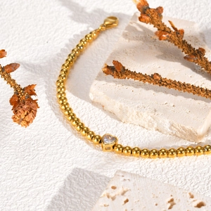 Detail van gouden kralenarmband met hartvormige zirkoon op witte stenen achtergrond