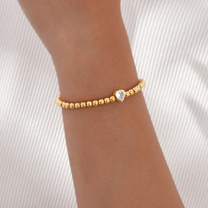 Gedetailleerd beeld van goudkleurige kralenarmband met een hartvormige zirkoon
