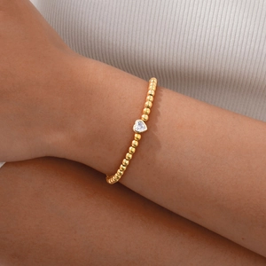 Gouden kralenarmband met hartvormige zirkoon hanger gedragen over witte kleding