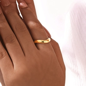 Gros plan d'une bague dorée ondulée minimaliste sur un doigt avec une finition polie