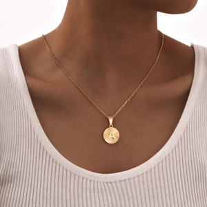 Dettaglio di una collana d'oro con ciondolo lettera A e incisione a raggiera su modella