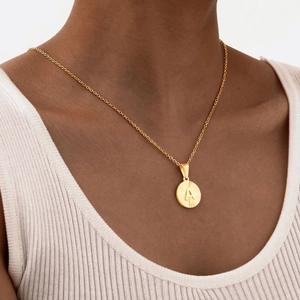Collana con ciondolo rotondo dorato con lettera A e trama a raggiera indossata
