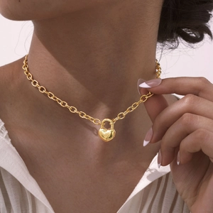 Dettaglio ravvicinato di una collana con lucchetto a cuore in acciaio dorato su modella