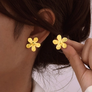 Goldene Edelstahl-Blumenohrstecker mit strukturierten Blütenblättern am Model getragen