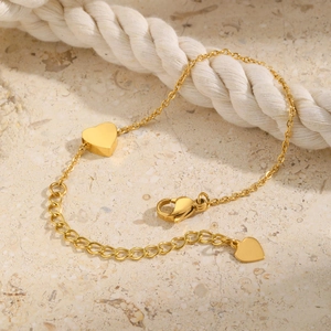 Detail of golden stainless steel heart anklet with lobster clasp on stone surface