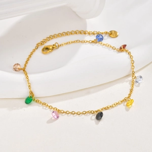 Golden stainless steel anklet with multi-colored zircon stones on a minimalist background