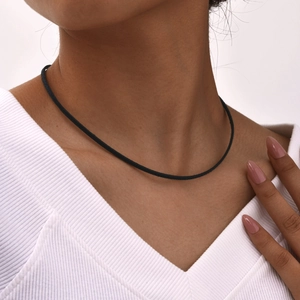 Dettaglio di un choker nero minimalista su una modella che indossa un top bianco a V