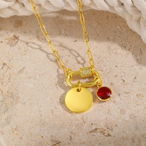 Detail of paperclip chain necklace with gold disc and red gemstone pendant on stone background