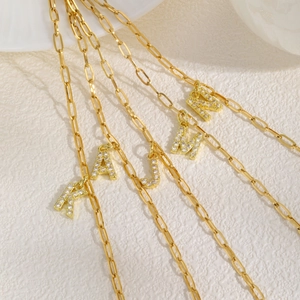 Detail van gouden paperclip ketting armbanden met pavé zirkonia letter hangers