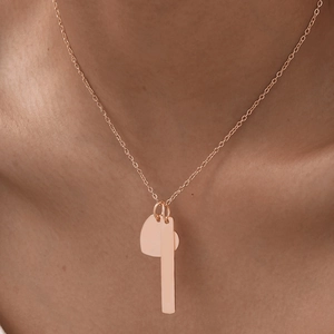 Minimalist rose gold necklace with bar and heart pendants shown on a female model