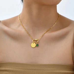 Detail of gold rectangular link chain with a green gemstone charm and circular pendant