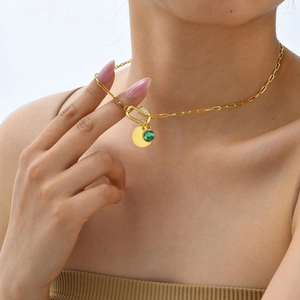 Macro shot of gold paperclip chain necklace with green zircon pendant and gold coin