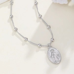 Macro-detail van zilveren Maagd Maria-hanger aan een slangenketting met kleine metalen kralen