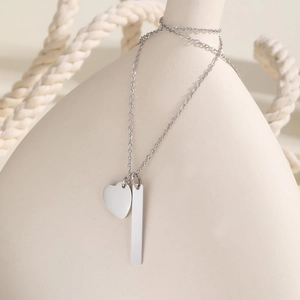 Detail of silver bar and heart pendants on necklace draped over ceramic vase