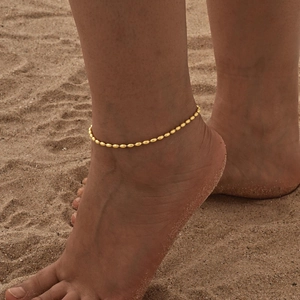 Detail einer goldenen Perlen-Fußkette am Sandstrand, die ihre Metallstruktur hervorhebt