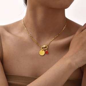 Gold paperclip chain necklace with red gemstone and round pendant on model