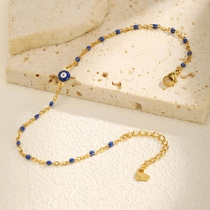 Cavigliera in acciaio dorato con occhio greco e perle blu su sfondo di pietre