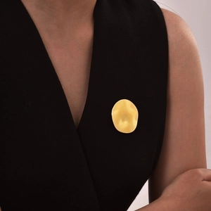 Detail of a gold irregular round brooch with ripple texture on a black V-neck top