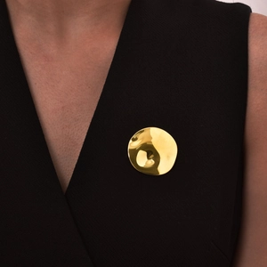 Detail view of irregular textured gold round brooch pinned on a black V-neck garment