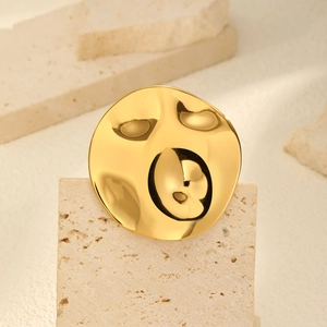 Detail of golden irregular round brooch with textured hammered finish on beige stone
