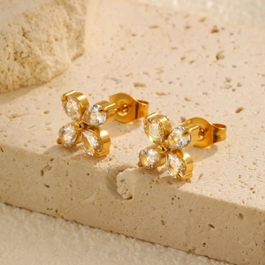 Detailed close-up of golden four-leaf flower stud earrings with clear zircon stones