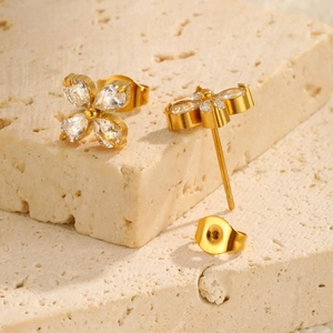 Close-up of gold-plated flower stud earrings with zircon petals on a beige stone