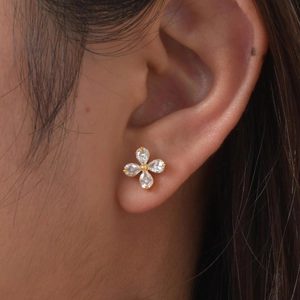 Close-up of four-leaf flower gold stud earrings with white marquise zircons on ear