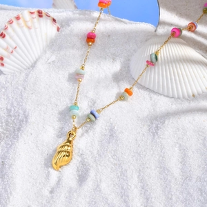 Detail of gold seashell pendant with colorful beads on white sand beach background