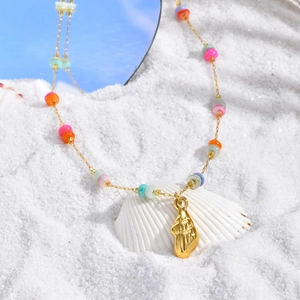 Golden ocean shell necklace with colorful beads on beach sand with blue sky reflection