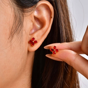 Close-up of golden four-leaf flower earrings with red drop-shaped stones on a model ear