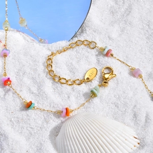 Detail of gold seashell necklace with colorful stones on white beach sand