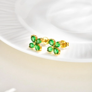 Detailed view of golden flower earrings with green pear-cut zircon on a white plate
