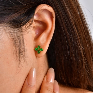 Detailed close-up of a gold flower stud earring with green pear-shaped gemstones on model