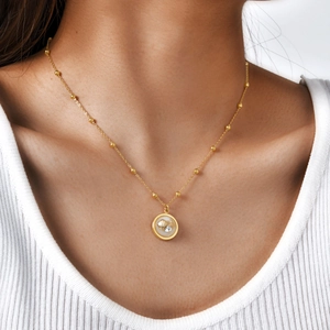 Detail of gold shell pendant necklace with mother of pearl and bead chain on model