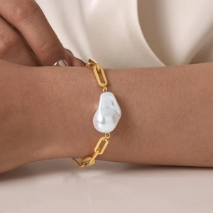 Dettaglio del bracciale vintage a maglie larghe dorate con una grande perla barocca al polso