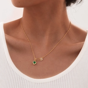 Detail of gold safety pin heart pendant with green gemstone on woman neck